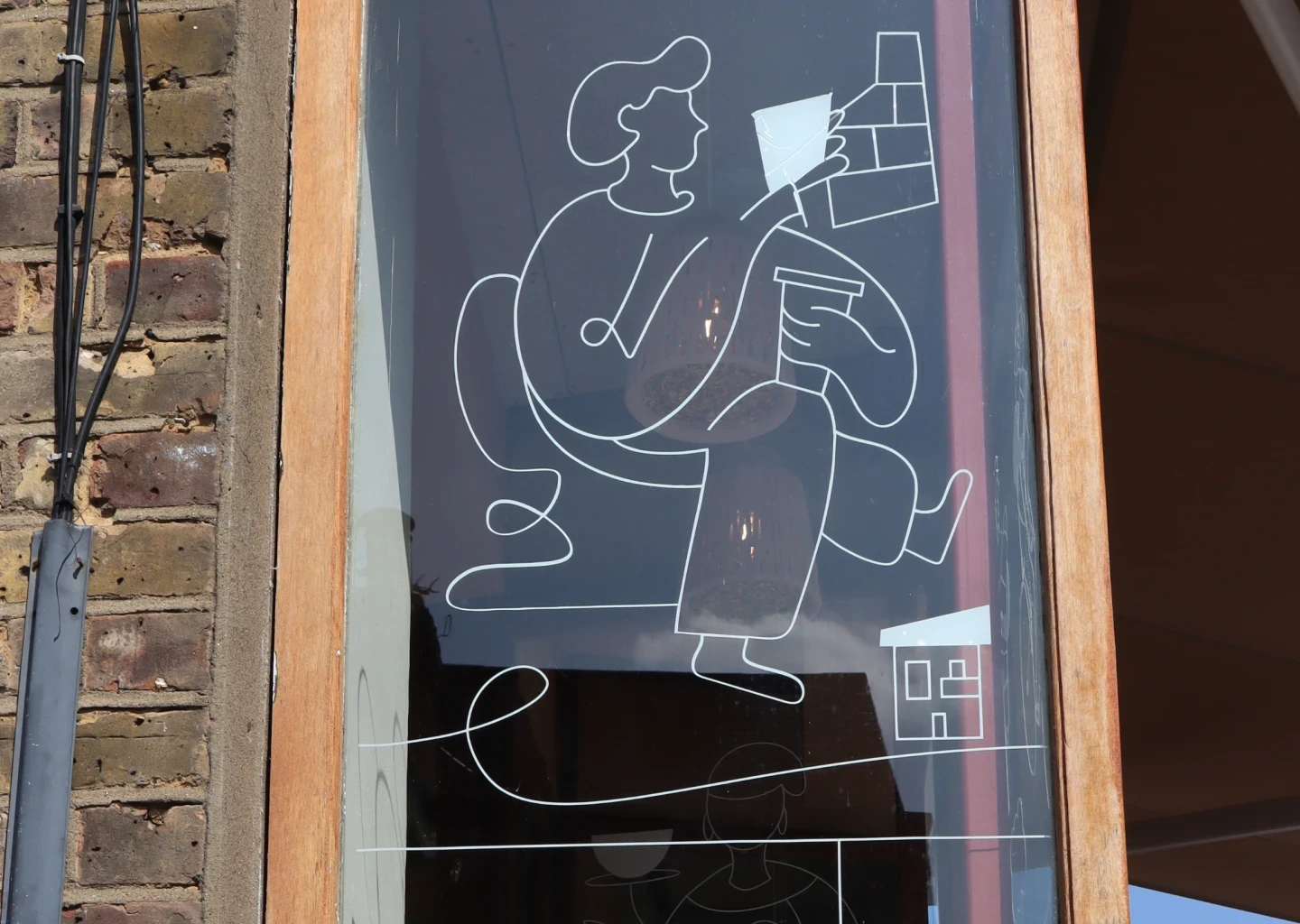 Line art illustration of a person with tools applied on a café window at Clay & Bean, viewed from outside.