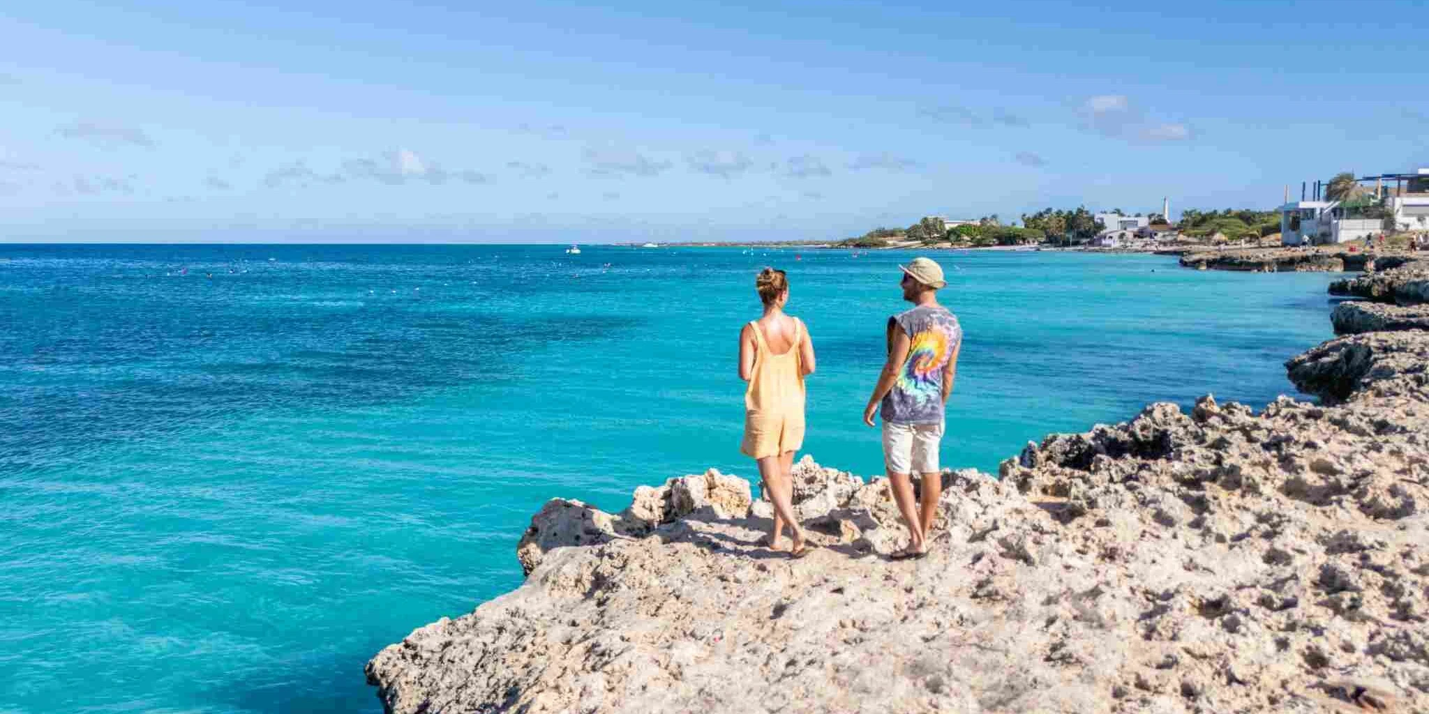 a couple standing on rocky shore by the sea in the Caribbean, having purchased hurricane travel insurance to protect their trip