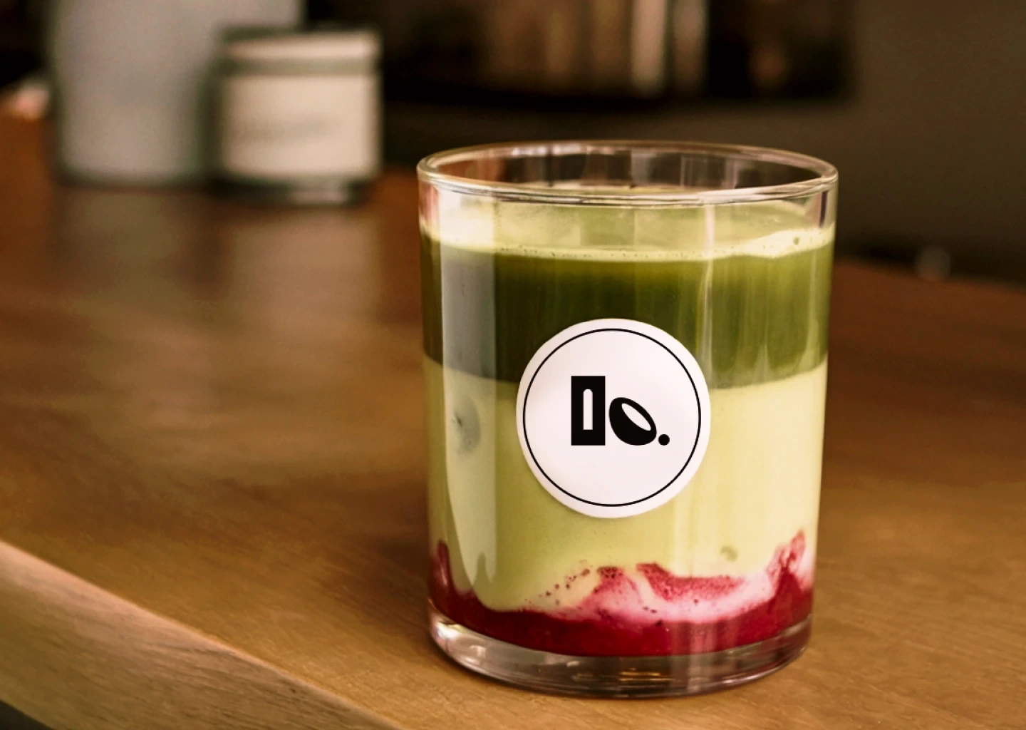 Layered iced matcha latte with berry base served in a glass featuring the Clay & Bean logo sticker