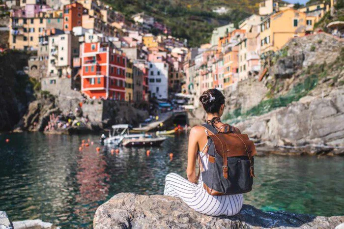 a young female traveler sitting on a rock overlooking a peaceful lake, indicating the need to buy travel insurance for Italy before exploring the country