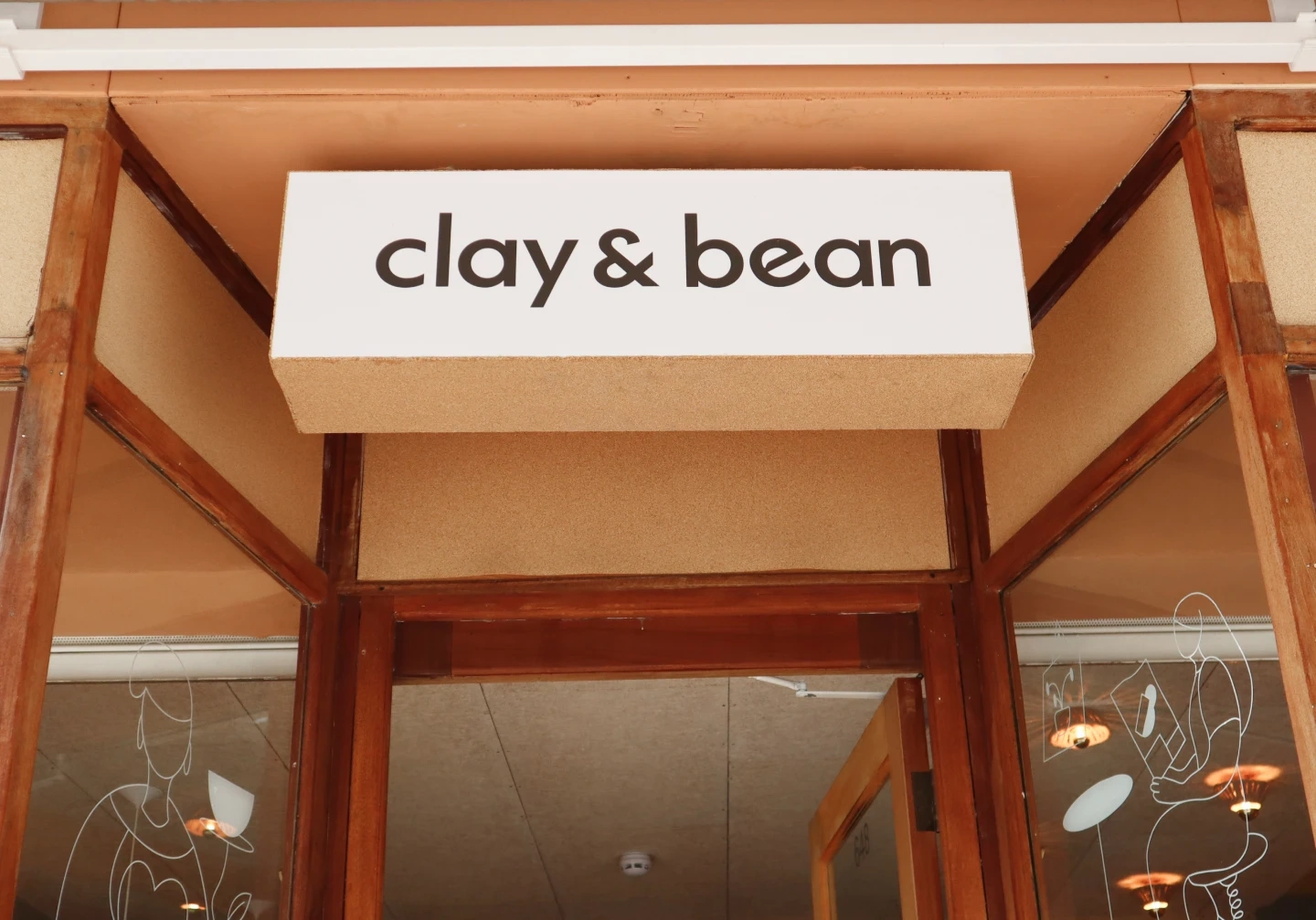 Clay & Bean exterior sign with bold black logotype mounted above café entrance framed in wood and glass.