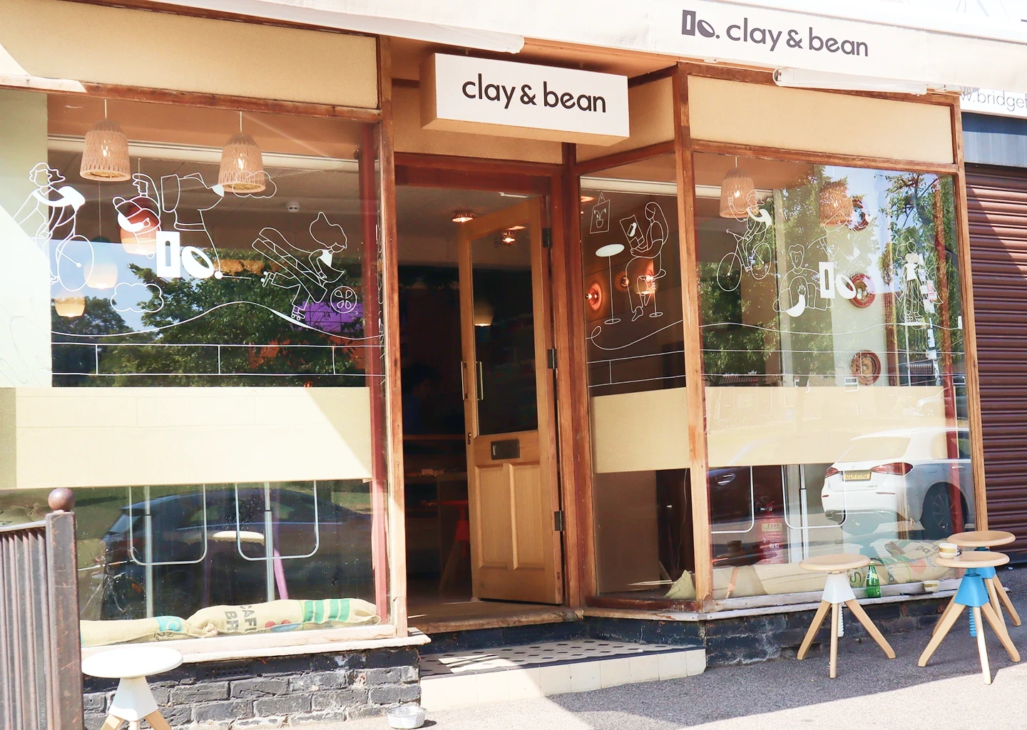 Clay & Bean coffee shop exterior with glass illustrations, logo signage, and wooden frame
